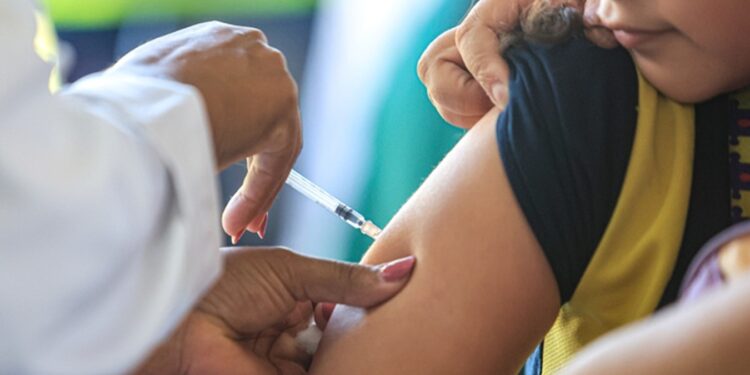 Imagem ilustrativa de profissional de saúde aplicando vacina no braço de uma criança em posto de atendimento, em referência ao Dia D de vacinação promovido pelo SUS
