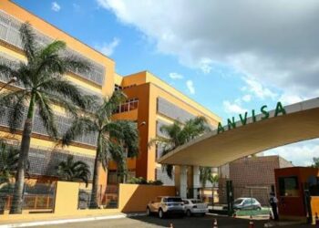 Fachada do prédio da Anvisa, a Agência Nacional de Vigilância Sanitária, com o letreiro verde na entrada, palmeiras e céu de nuvens, órgão responsável por esclarecer boatos sobre alimentos