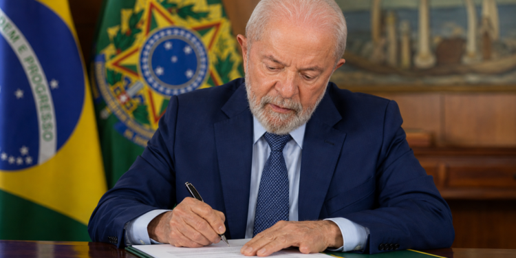 Imagem ilustrativa do presidente da República assinando documento no gabinete, ao lado da bandeira nacional, em referência ao anúncio sobre o fim da taxa das blusinhas nas compras internacionais