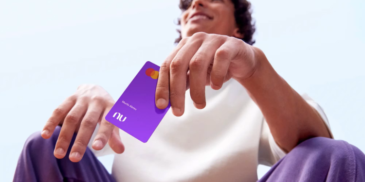 Imagem ilustrativa de homem sentado ao ar livre segurando um cartão de crédito roxo do Nubank, em referência ao Novo Desenrola Brasil 2026 e à recuperação do limite após a renegociação