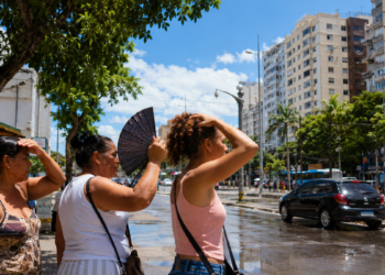 Imagem ilustrativa de pessoas se abanando e cobrindo a cabeça do sol forte em uma avenida arborizada de céu azul, referência ao contraste de clima entre as regiões durante a virada do tempo