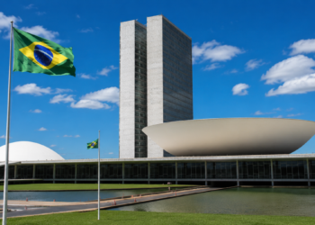 Fachada do Congresso Nacional com a bandeira do Brasil hasteada em primeiro plano, em imagem ligada à aprovação do projeto que dá prioridade no Bolsa Família a vítimas de violência doméstica.