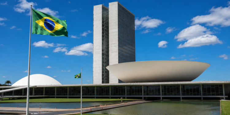Fachada do Congresso Nacional com a bandeira do Brasil hasteada em primeiro plano, em imagem ligada à aprovação do projeto que dá prioridade no Bolsa Família a vítimas de violência doméstica.