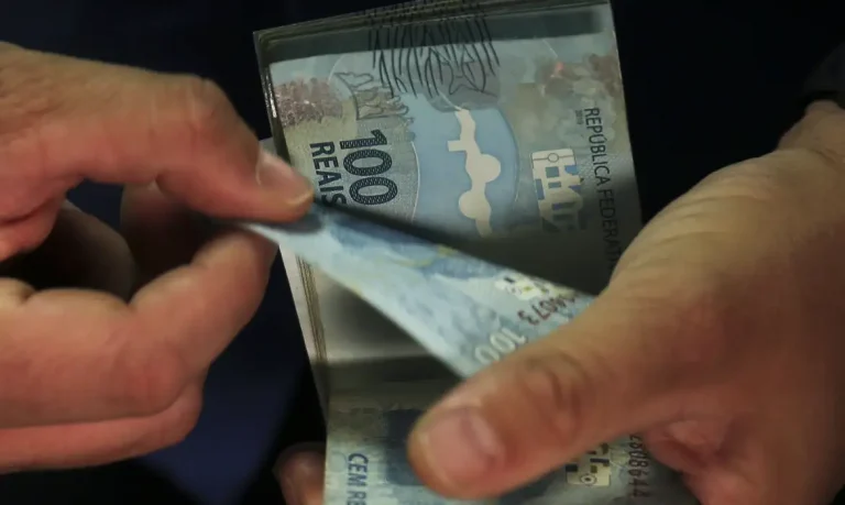 Imagem ilustrativa de mãos manuseando notas de cem reais, em referência aos benefícios que acompanham o valor do salário mínimo