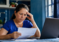 Imagem ilustrativa de mulher lendo um documento diante de um notebook, com a mão apoiada na cabeça, cena ligada à negativa de benefício do INSS tratada em projeto de lei.