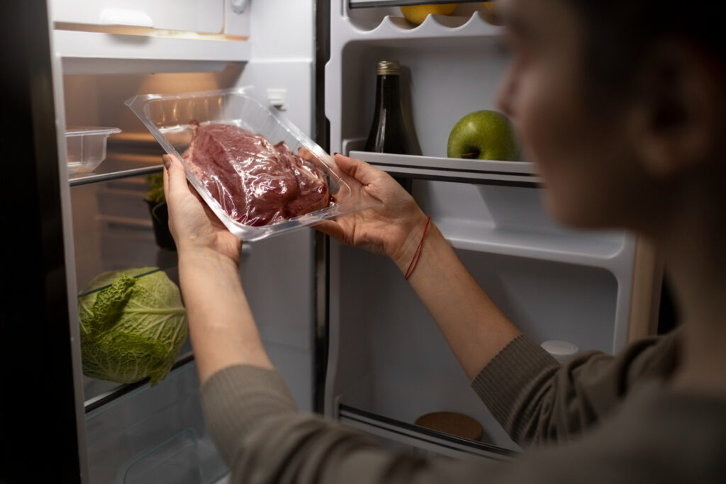 Imagem ilustrativa de pessoa retirando uma bandeja de carne suína embalada da prateleira da geladeira, tema da orientação sobre o que fazer com o produto suspenso.