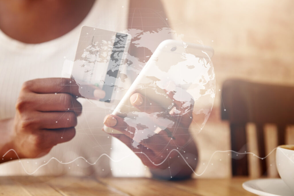 Imagem ilustrativa de pessoa segurando cartão e celular durante compra on-line, com globo terrestre digital sobreposto, em referência aos tributos cobrados nas compras internacionais