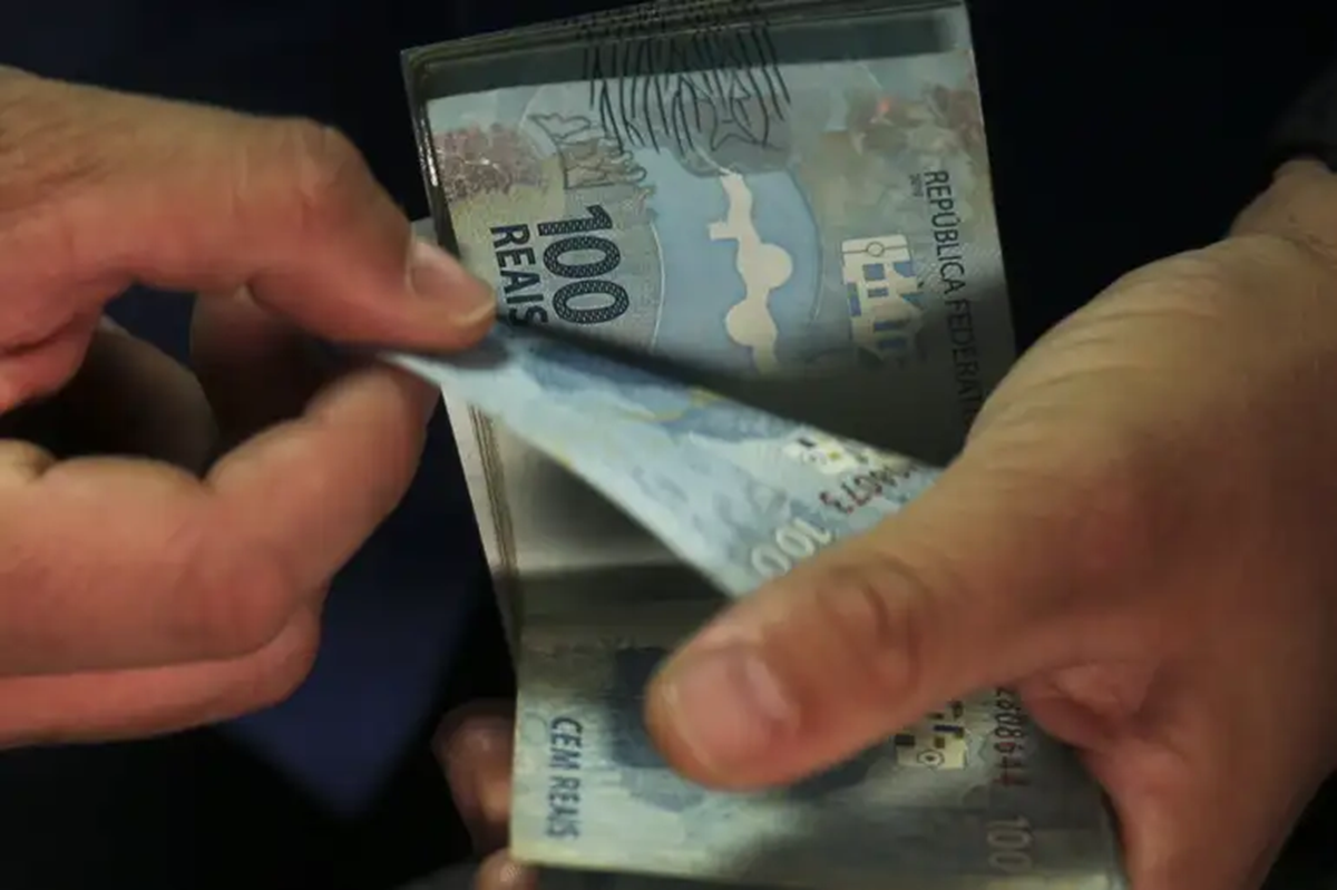 Mãos contando um maço de cédulas de cem reais, referência ao cálculo do valor disponível para saque conforme o saldo do fundo