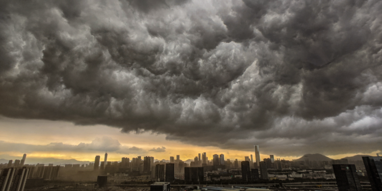Nuvens de tempestade densas avançam sobre cidade ao entardecer.