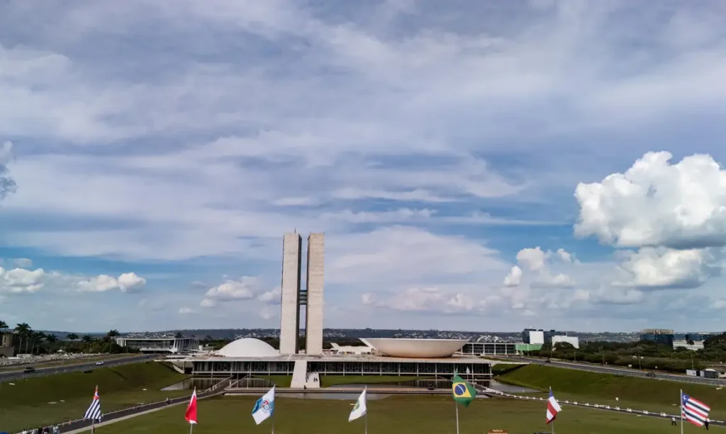 Vista aérea do Congresso Nacional, em Brasília, com as duas torres ao fundo e bandeiras de estados brasileiras hasteadas em primeiro plano.