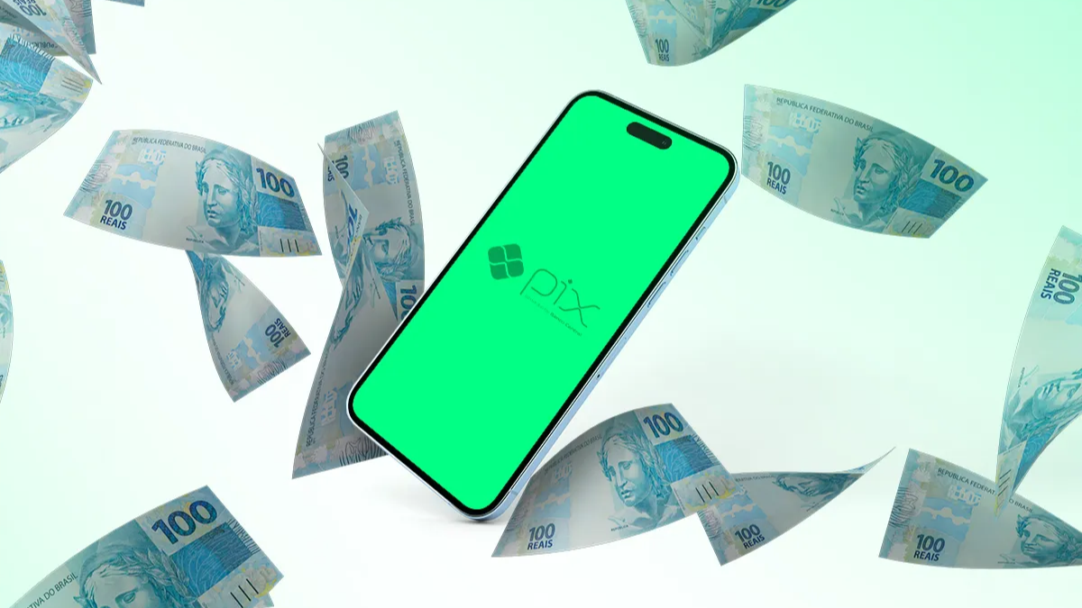 Celular com tela verde Pix cercado por notas de cem reais voando em fundo claro.