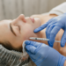 Aplicação de botox facial em clínica estética por profissional com luvas azuis.