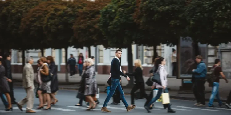 Pessoas atravessam rua movimentada indo ao trabalho em centro urbano.