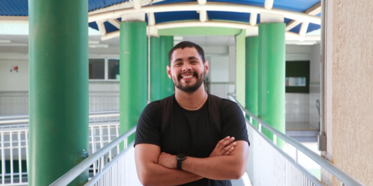 Estudante sorridente no corredor da faculdade com mochila e camiseta preta.