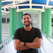 Estudante sorridente no corredor da faculdade com mochila e camiseta preta.