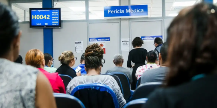 Pessoas sentadas aguardam atendimento em sala de perícia médica do INSS.