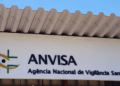 Fachada da ANVISA com logotipo verde e amarelo e letreiro da Agência Nacional de Vigilância Sanitária.