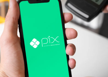 Mão segura smartphone com tela verde do Pix, próximo a máquina de cartão de crédito.