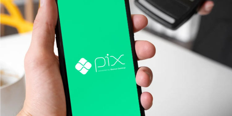 Mão segura smartphone com tela verde do Pix, próximo a máquina de cartão de crédito.