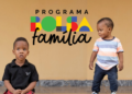Dois meninos pequenos, um sentado e outro em pé, com logo do Bolsa Família ao fundo.
