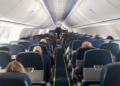 Passageiros sentados em cabine de avião comercial em voo diurno.