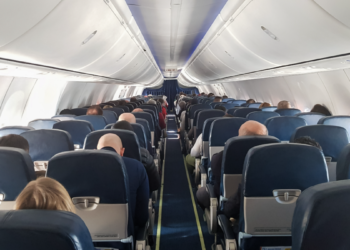 Passageiros sentados em cabine de avião comercial em voo diurno.