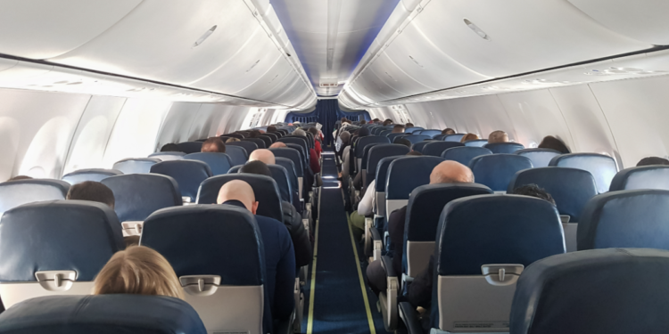 Passageiros sentados em cabine de avião comercial em voo diurno.