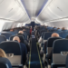 Passageiros sentados em cabine de avião comercial em voo diurno.