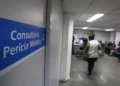 Sinalização "Consultório Perícia Médica 2" e pessoas aguardando em sala de espera ampla.