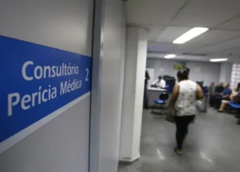 Sinalização "Consultório Perícia Médica 2" e pessoas aguardando em sala de espera ampla.