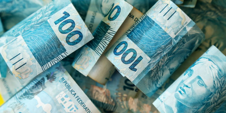 Notas de cem reais brasileiras em destaque sobrepostas.