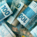 Notas de cem reais brasileiras em destaque sobrepostas.