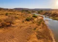 Região rural seca, com solo rachado e rio com pouca água sob forte sol.