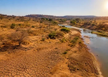 Região rural seca, com solo rachado e rio com pouca água sob forte sol.
