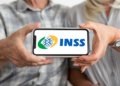 Duas pessoas seguram celular exibindo logo do INSS, foco nas mãos e aparelho.