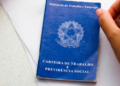 Mão segurando caneta próxima à Carteira de Trabalho e Previdência Social azul.