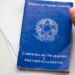 Mão segurando caneta próxima à Carteira de Trabalho e Previdência Social azul.