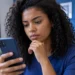 Pessoa consulta smartphone para acompanhar alertas e serviços digitais da Justiça Eleitoral pelo e-Título