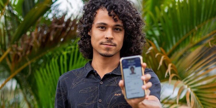 Jovem mostra a tela do celular com o e-Título, documento digital do eleitor, em meio a folhagens
