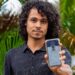 Jovem mostra a tela do celular com o e-Título, documento digital do eleitor, em meio a folhagens