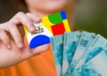 Imagem ilustrativa de pessoa segurando o cartão do Programa Bolsa Família ao lado de cédulas de cem reais em leque.