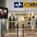 Clientes e funcionários dentro de uma agência dos Correios, com o letreiro da estatal acima dos guichês de atendimento.
