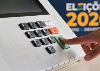 Imagem ilustrativa: dedo aperta a tecla confirma da urna eletrônica em arte das Eleições 2026, sobre o voto facultativo