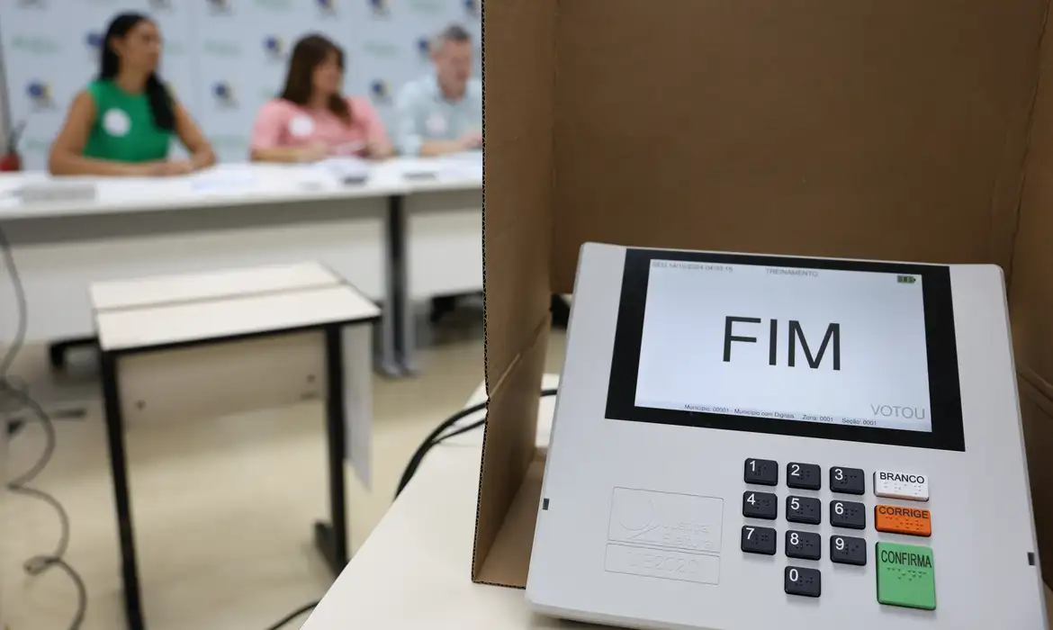 Urna eletrônica e equipe eleitoral representando os convocados pela Justiça Eleitoral nas eleições de 2026.