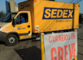 Imagem ilustrativa: caminhão amarelo do Sedex atrás de uma faixa com os dizeres Correios em greve, cena que remete ao impacto da greve dos Correios nas entregas da Shein