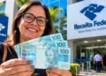 Contribuinte segura cédulas de reais em frente à Receita Federal, representando a liberação do lote residual de restituição do Imposto de Renda 2026.