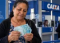 Beneficiária confere notas de R$ 100 em agência bancária, representando o pagamento do BPC.
