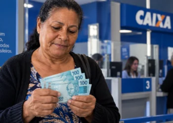 Beneficiária confere notas de R$ 100 em agência bancária, representando o pagamento do BPC.
