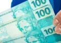 Mão segurando notas de real representa o valor disponível para retirada pelo saque-aniversário do FGTS.