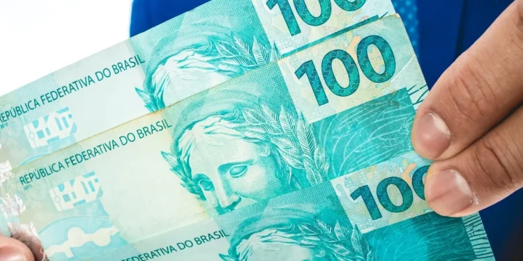 Mão segurando notas de real representa o valor disponível para retirada pelo saque-aniversário do FGTS.